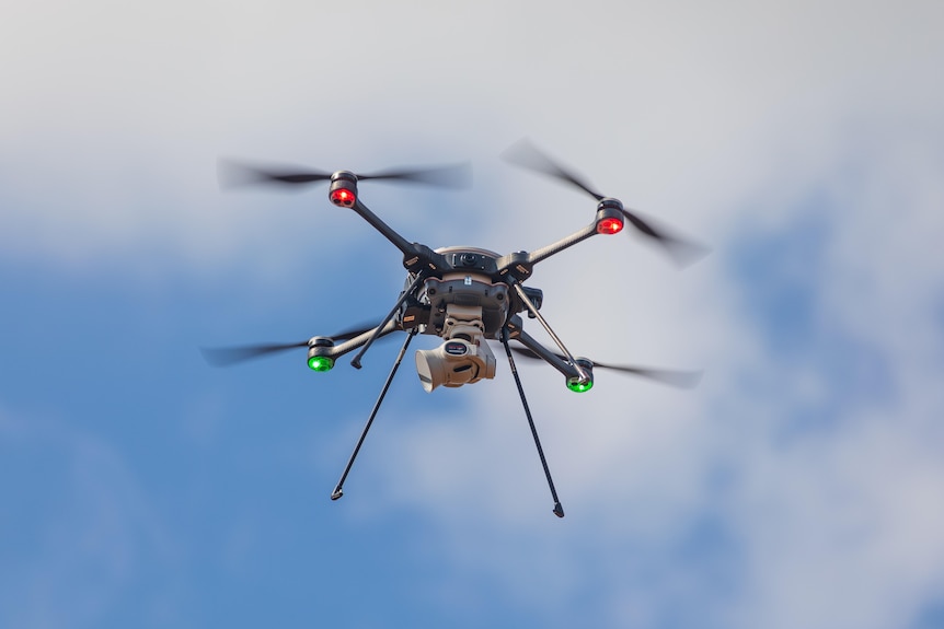 A close-up of a small drone as it flies in mid-air, its rotors are blurry as they spin