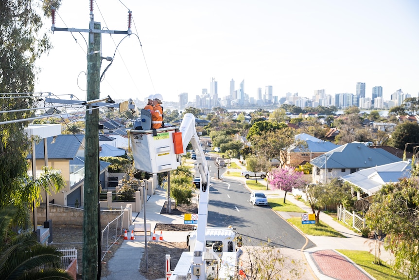 High-vis workers on a cherry picker next to power lines with Perth skyline in the background.