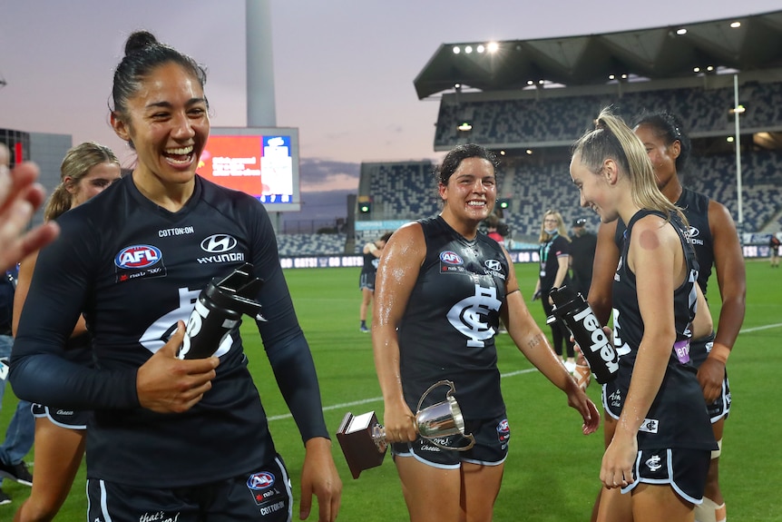 Darcy Vescio (left) smiles while holding their water bottle. In the background, Maddy Prespakis and Georgia Gee smile.