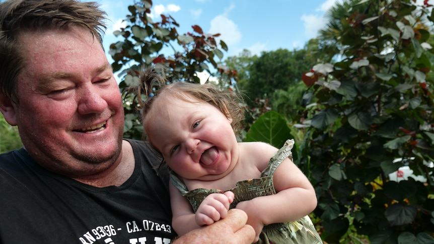A father and his daughter laughing together in a garden.