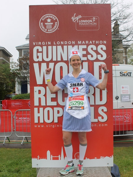 A woman standing on a podium wearing a short blue dress, a nurse cap and running shoes.