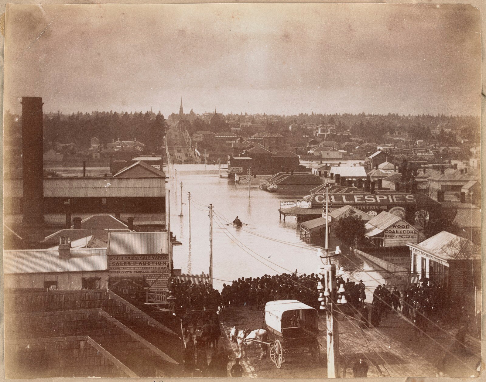 A sepia toned photograph shows a flooded main road, a figure in a rowboat in the middle of the street