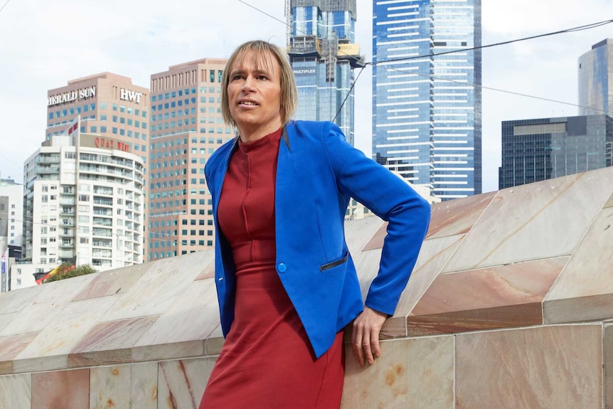Transgender activist Melissa Griffiths wearing office attire and standing against sandstone wall with city in background.