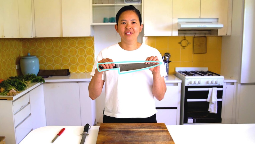 Thi Le stands in a home kitchen holding a chef's knife, for a story about knife techniques.