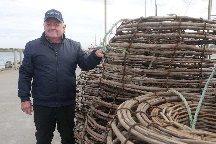 A fisherman stands next to a pile of lobster pots.