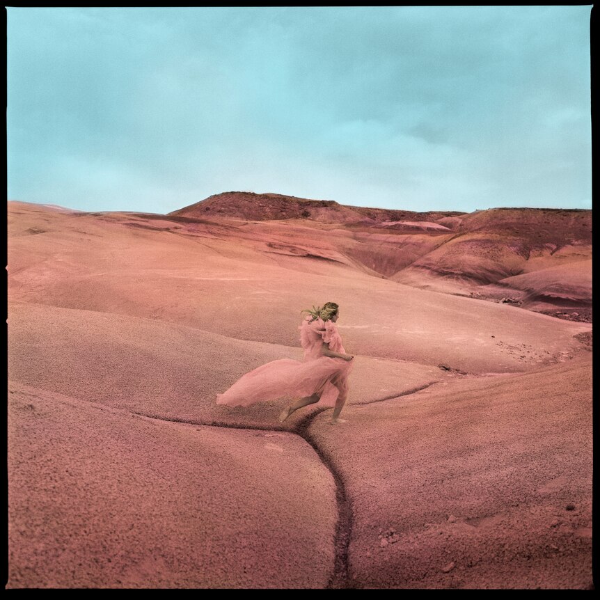 a woman in an elegant pink dress dancing in the middle of a desert