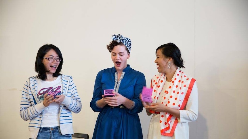 Three women from the Geek Girl Academy look at their phones.