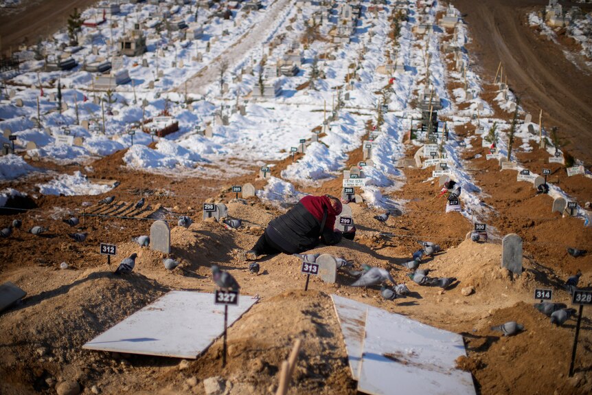 A woman cries over the graves of her son and her daughter in a large cemetary.