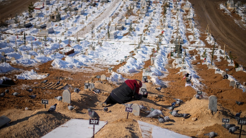 A woman cries over the graves of her son and her daughter in a large cemetary.