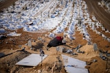 A woman cries over the graves of her son and her daughter in a large cemetary.