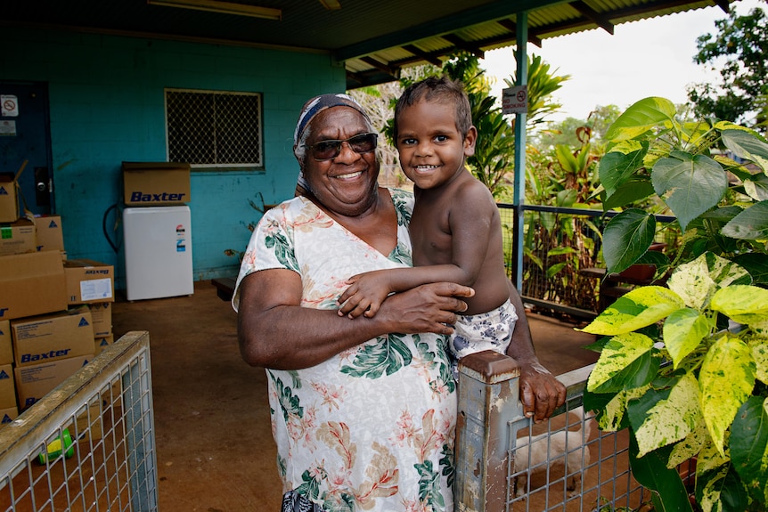 an aboriginal woman smiling in a dress holding a baby