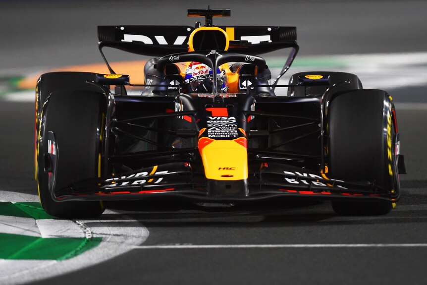 Max Verstappen in a dark blue Red Bull, during a night race in Saudi Arabia, going through a corner.