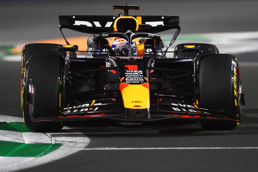Max Verstappen in a dark blue Red Bull, during a night race in Saudi Arabia, going through a corner.