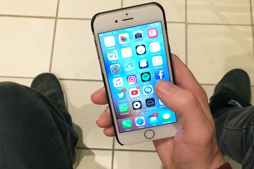 A unidentifiable man sits and uses his smartphone.