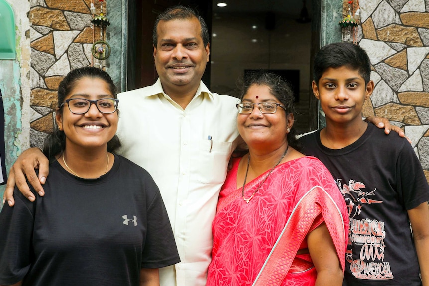 A husband and wife stand together with their teen daughter and son