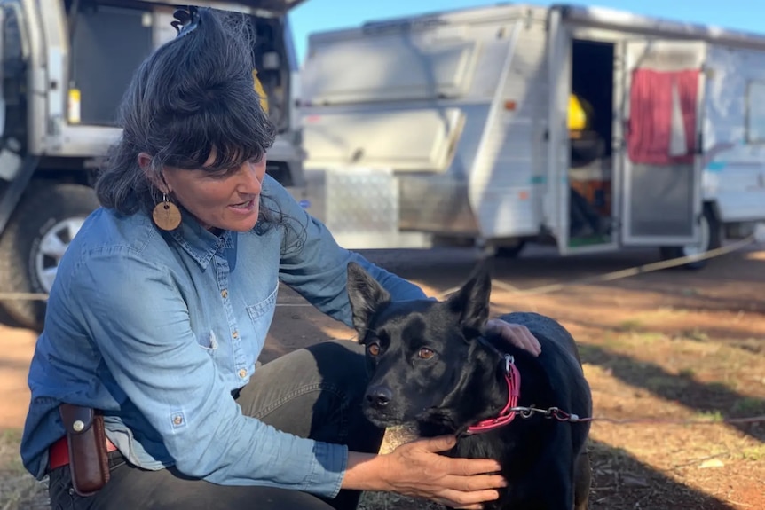A woman patting a dog outside a caravan.