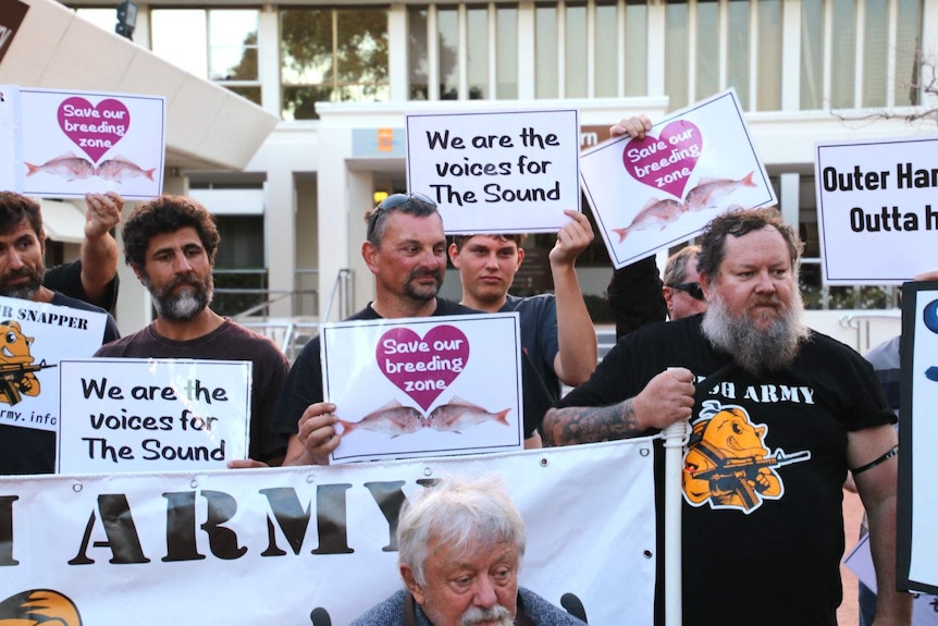 A group of men wearing 'Fish Army' shirts holding signs outside a council building which say "We are the voices for the Sound".