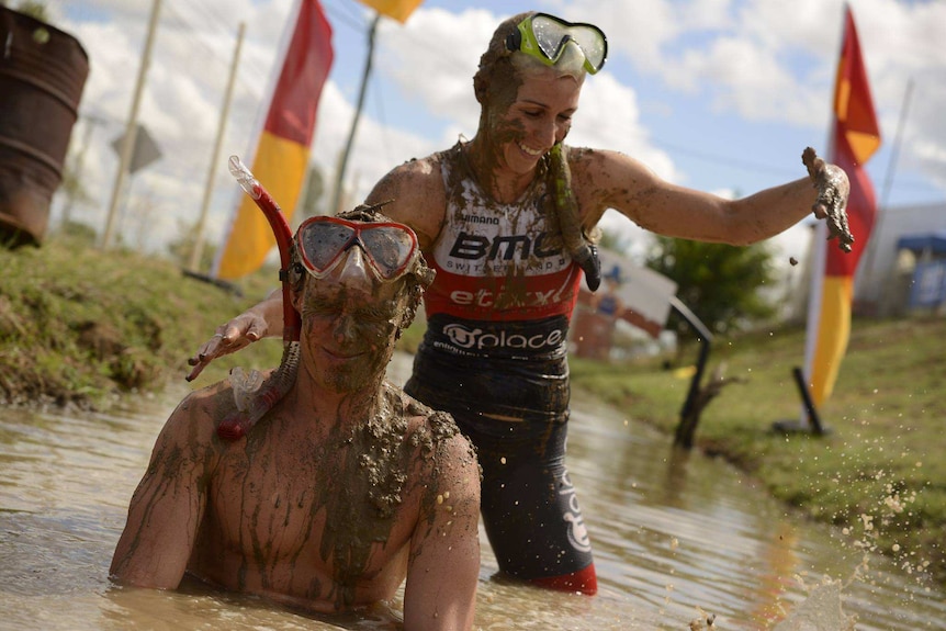 A woman puts mud onto the head of a man while bathing in a muddy creek