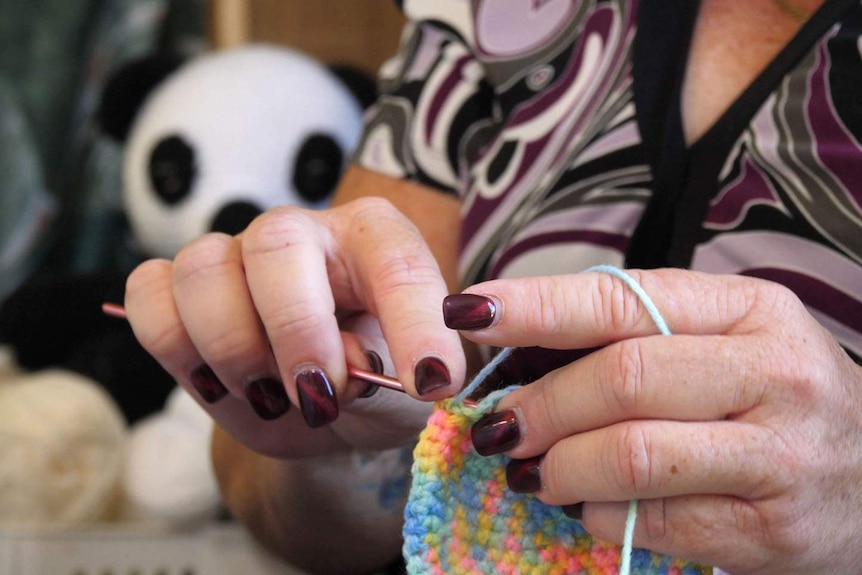 A woman with long maroon fingernails crochets brightly coloured wool
