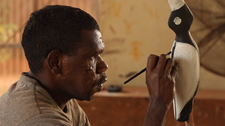 A Tiwi Islands artist paints a carved bird.