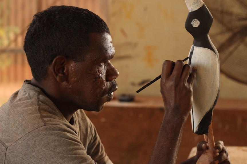 A Tiwi Islands artist paints a carved bird.