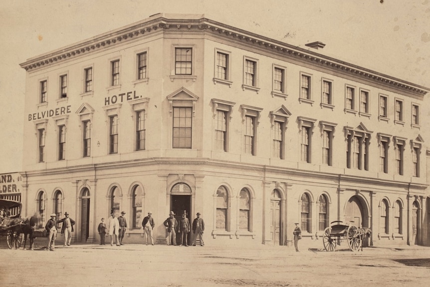 A 19th century sepia photo of a three-storey pub, with people and horses in front