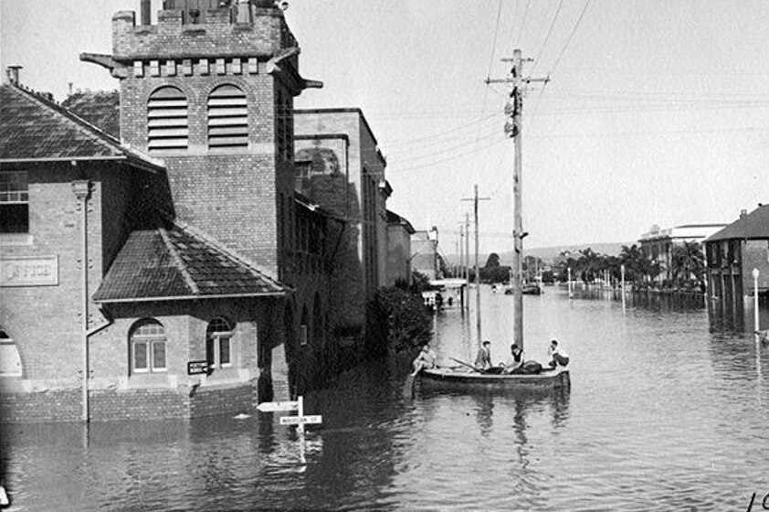 Old photo with flood waters coming up to bottom of a street sign in a main street of Lismore CBD.