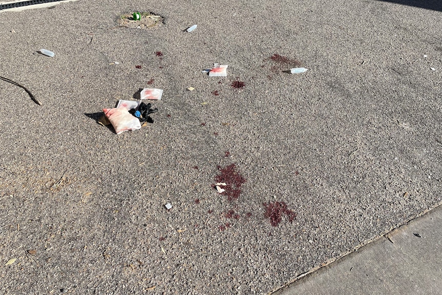 A number of blood spatters, with bloody gauze, black plastic gloves and empty saline bottles