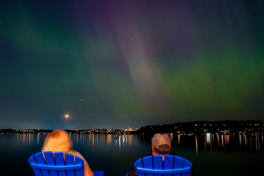 People sit in blue seats watching the aurora
