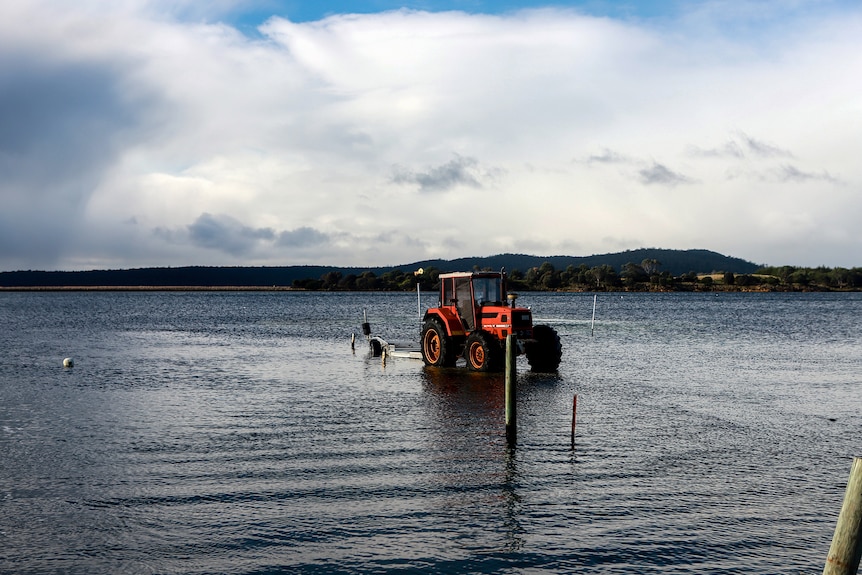 A red tractor sits in a bay with a small mountain in the background