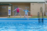 two primary school aged girls, sitting in bathers beside a pool with a sign which says 'Save Our Pool'