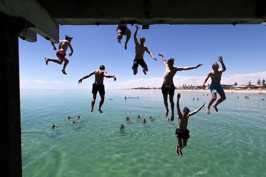 Boys jump off a jetty into the sea.