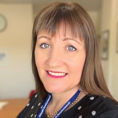 A woman stands smiling with a Queensland Health lanyard on.