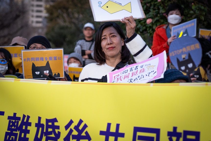 A woman at a protest holds up a sign with a fish on it.
