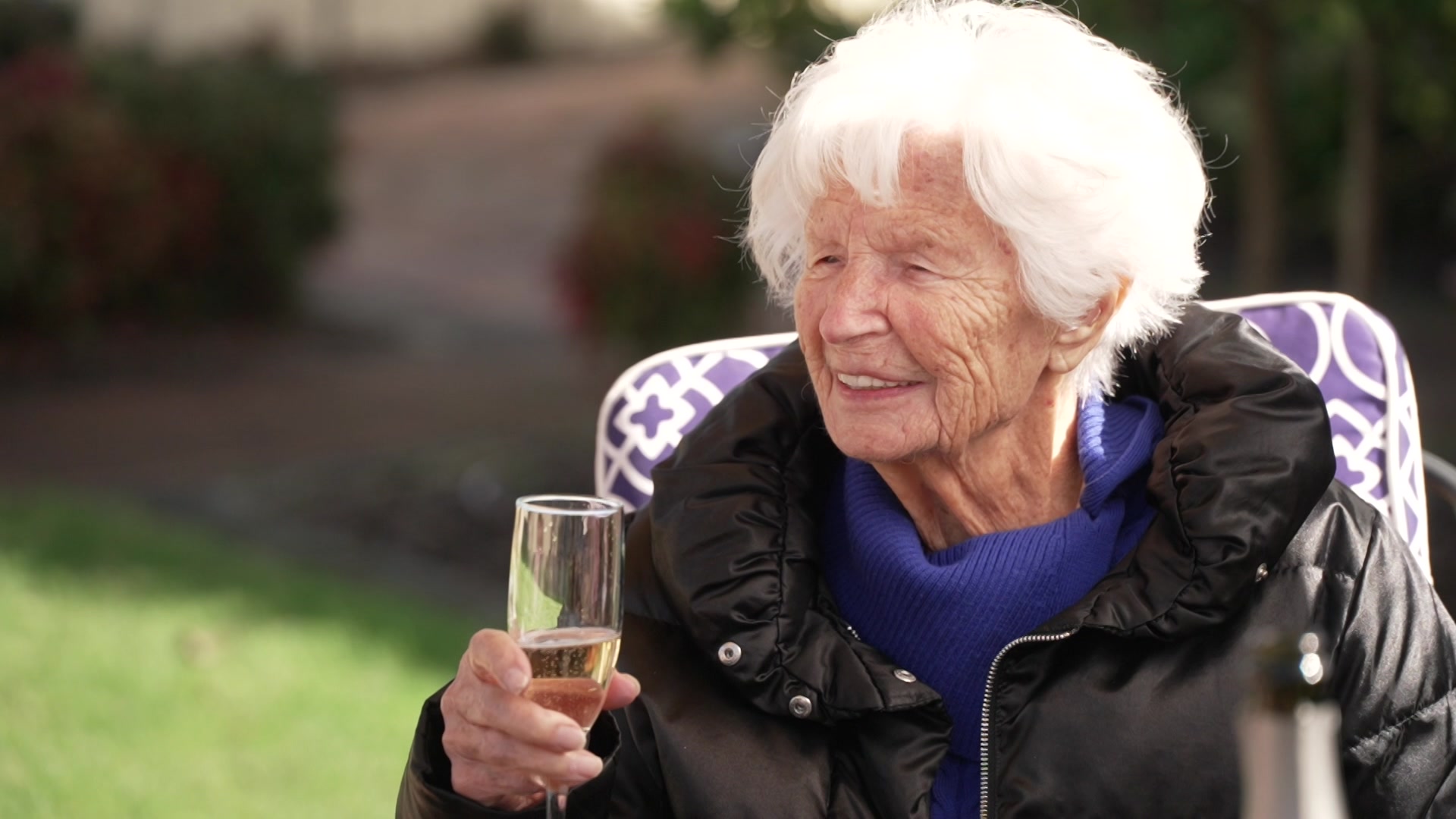 A woman sits in a chair outside with a glass of champagne in her hands