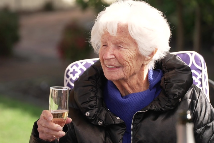 A woman sits in a chair outside with a glass of champagne in her hands