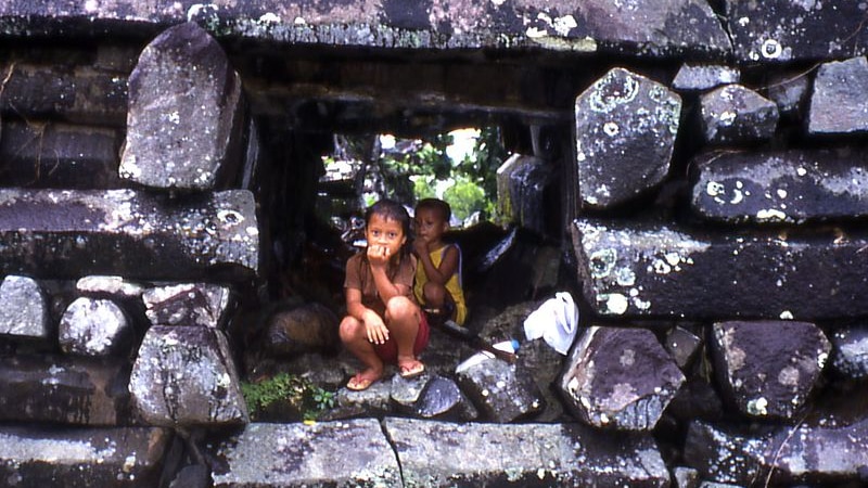 Two children in a passage hole through a thick basalt wall at Nan Modol, Pohnpei, Micronesia.