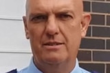 A bald police officer looks directly at the camera.