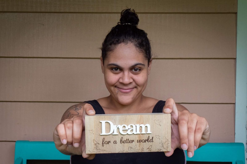 A young indigenous woman holding a sign toward camera saying Dream for a better world.