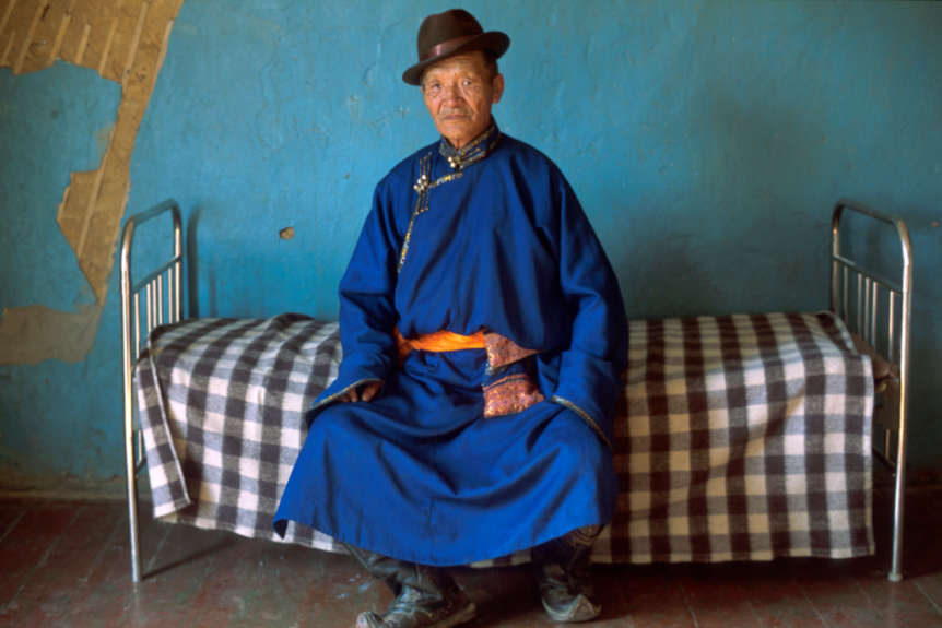A Mongolian man sitting on a bed.