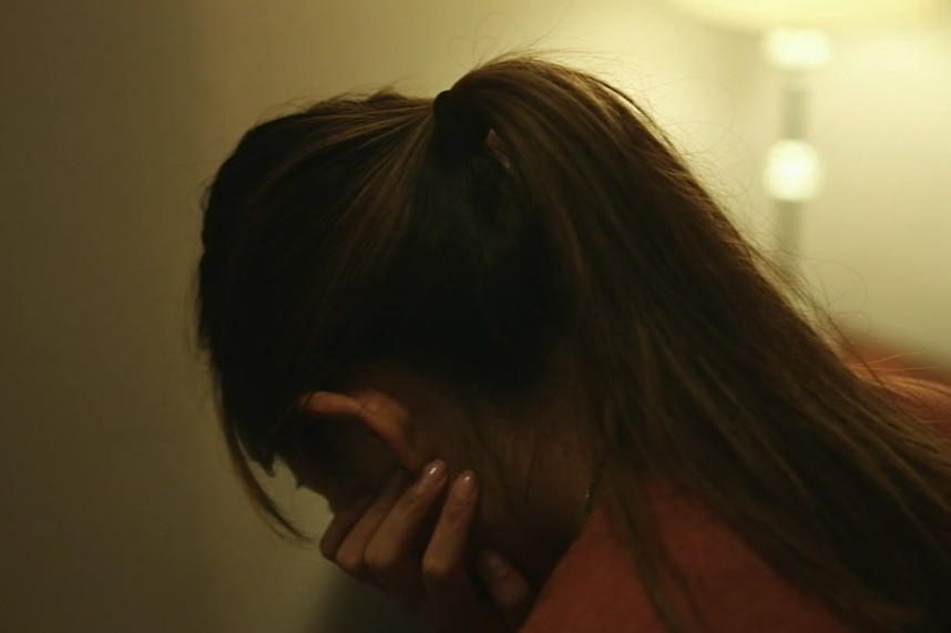 A woman in a darkened room with her head on her hand.