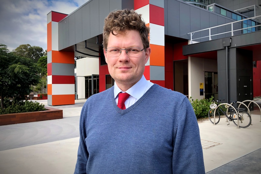 a brown haired man with glasses smiles at a camera