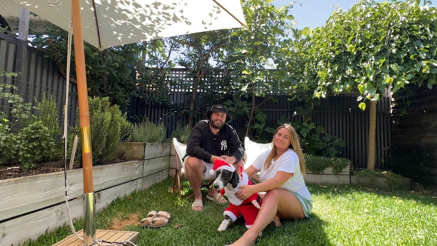 Two people smiling under an umbrella, cuddling a dog. 