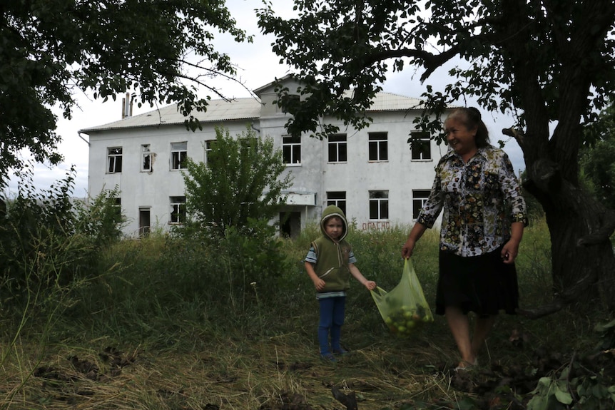 Small boy and older woman hold bag of apples in a garden