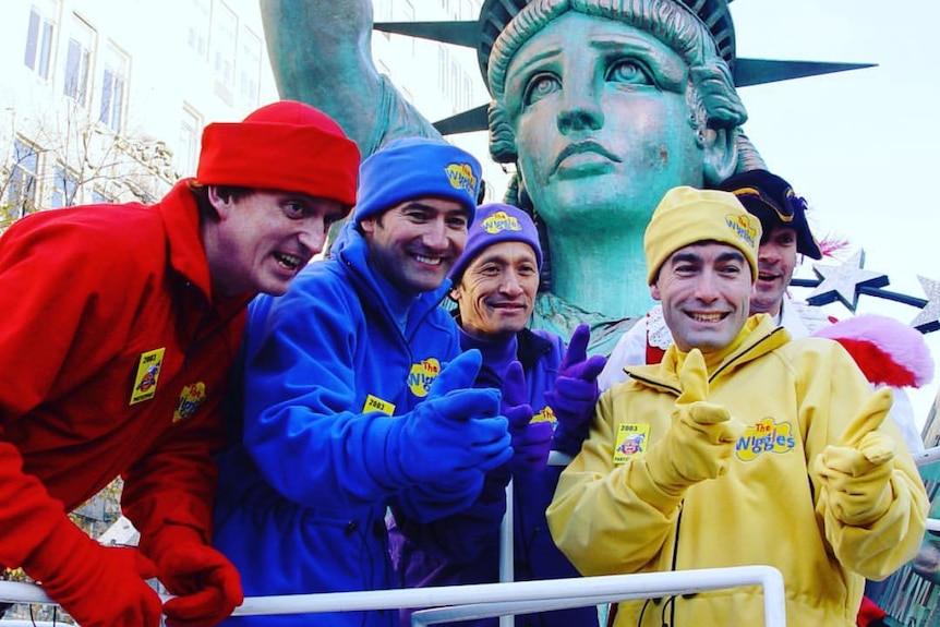 A photo from 2001 of the four members of The Wiggles wearing beanies, gloves and jackets in front of the statue of libertys head