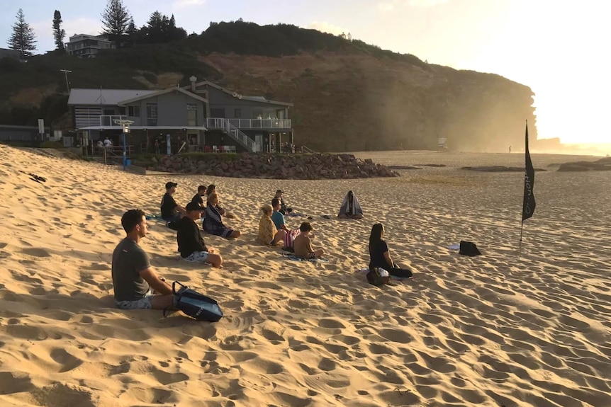 People sit on beach facing water watching the sunrise.