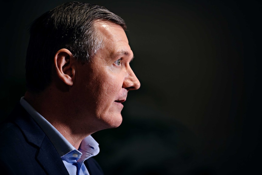 A side-on shot of Michael Gunner, wearing a suit jacket and navy shirt.