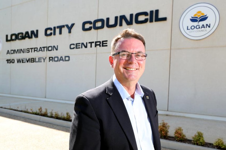 Logan City Council Mayor Luke Smith standing outside a building with the sign, Logan City Council Administration Centre.