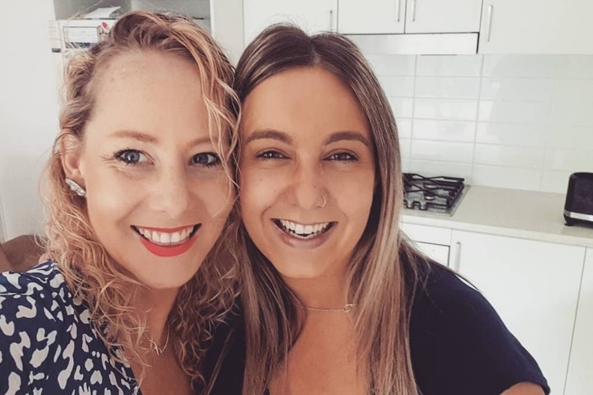 A photo of a smiling lesbian couple in a kitchen.