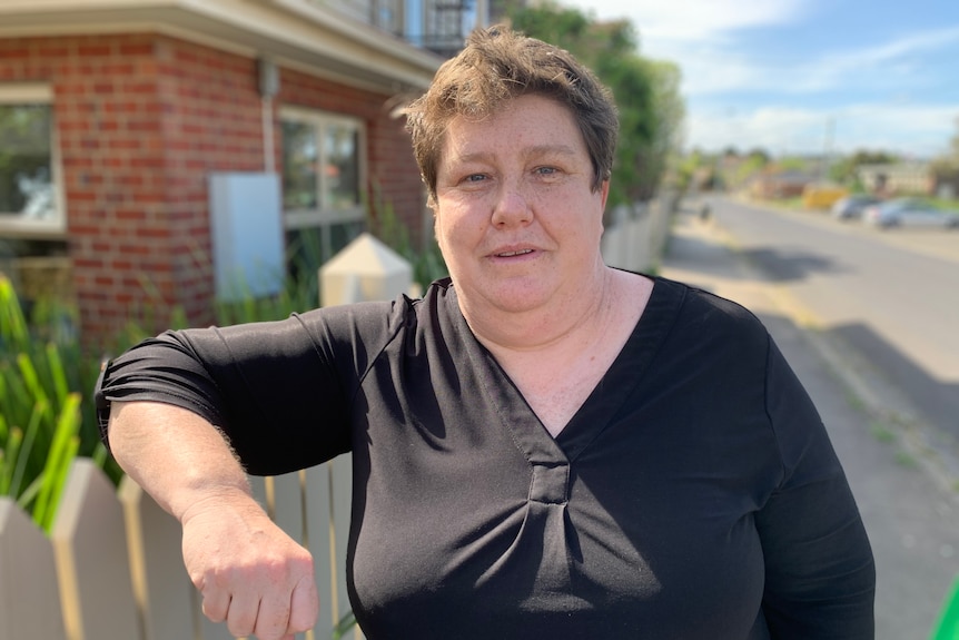 A woman stands resting her arm on a fence.